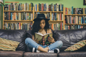 Woman in hat reading book on couch.
