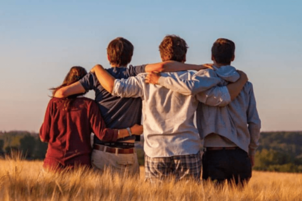 Four friends smiling and standing in a beautiful field, enjoying each other's company.