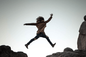Person leaping over rocks on mountain trail.